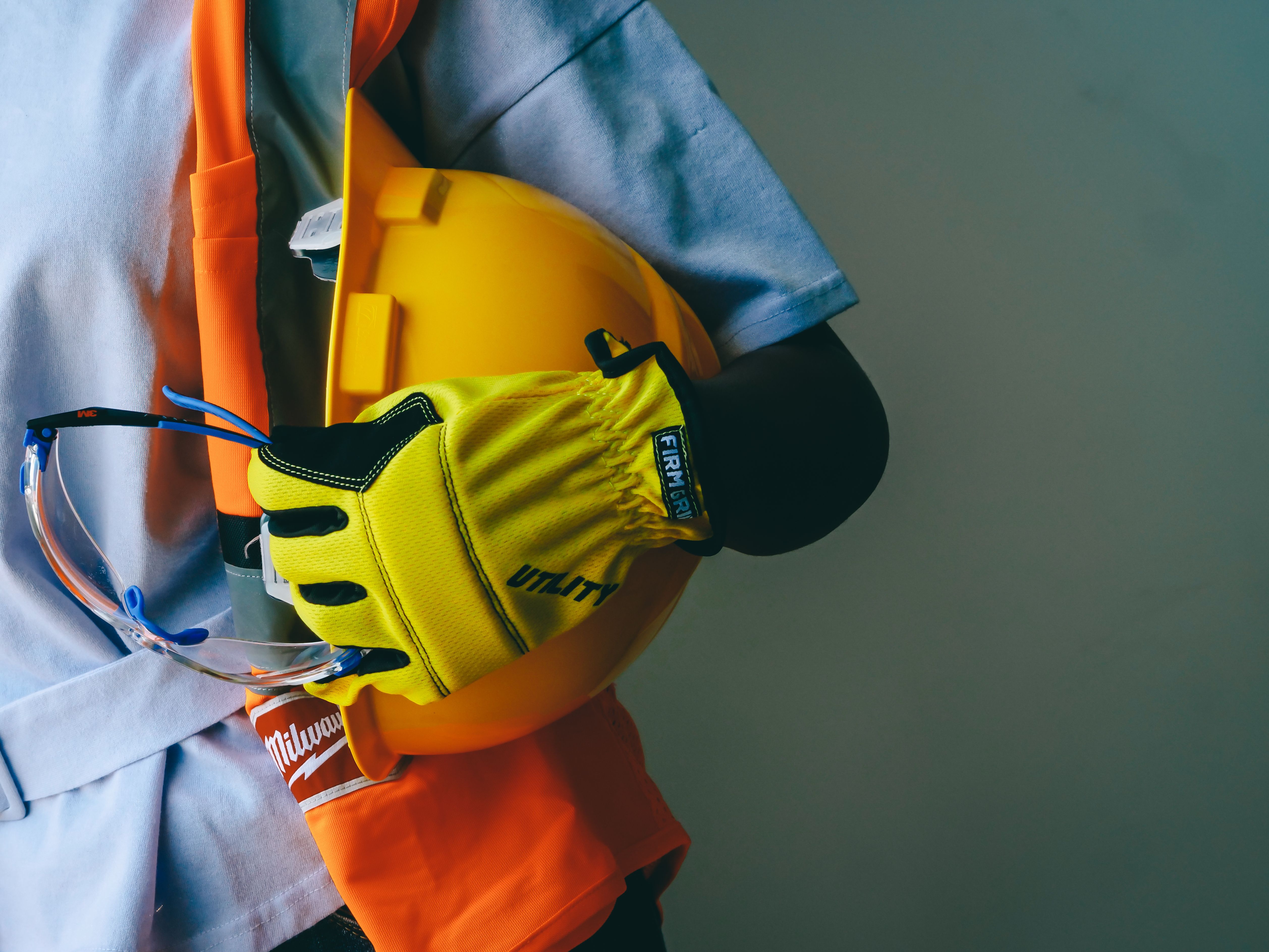 Worker holding a hard hat, safety glasses, and utility gloves